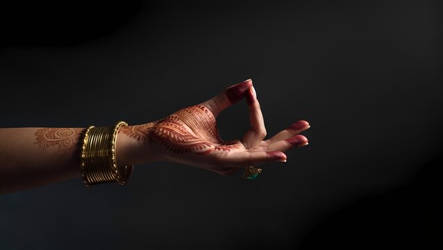 Bridal hand in symbolic dance mudra with henna and bangles on black background with copy space
