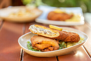 Close-up of a crispy vegetarian cordon bleu served on a rustic plate, filled with a creamy mushroom mixture and garnished with a lemon wedge. The dish is photographed outdoors in warm natural light, e