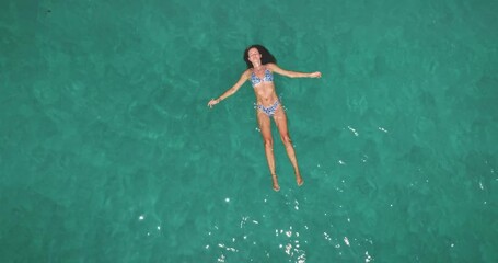 Young beautiful woman in bikini floats on her back in calm, transparent turquoise sea of Ko Lanta, feeling relaxed and enjoying peaceful summer vacation under the sun in Thailand. Top down aerial view