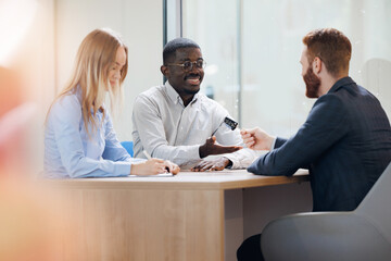 Seller of dealers gives keys to new car to happy young african american man and woman in auto showroom