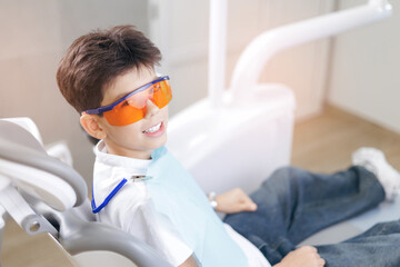Portrait caucasian cheerful boy smiling at dental clinic wearing protective glasses. Concept of no...