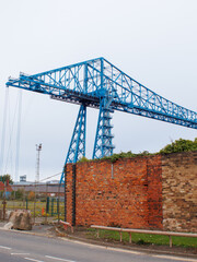 The Tees Transporter Bridge at Middlesbrough showing the structure and a old red industrial factory wall.
