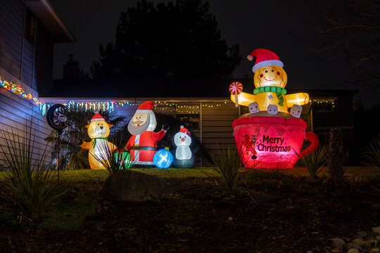 Inflatable glowing figure of Gingerbread man in cap with Santa hat near Sana, deer and penguin figures. Christmas decorated front yard