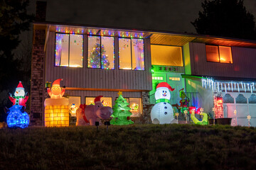 House with Christmass tree in the window and luminous inflatable figures decorating front yard at night. Christmas decoration of the house