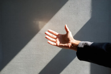 Hand shadow wall sunlight reaching gesture open human skin arm An open hand reaching toward faint shadow textured wall illuminated by sunlight streaming through window evoking hope and connection