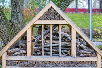 Decorative wooden insect hotel with compartments mounted in autumn park for supporting beneficial wildlife in Warsaw. High quality photograph.