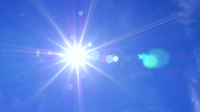 Bright sunshine with colorful lens flare moving across a clear blue sky with some soft white clouds, creating a vibrant and energetic background for concepts of hope, summer, and nature