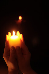 Hands holding burning candle in dark. Selective soft focus, blur smoke black, brown, yellow background.