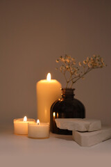 Selective soft focus burning blur Candles with flower, stones podium. Evening night Light and shadow gray neutral background. Minimalist still life.