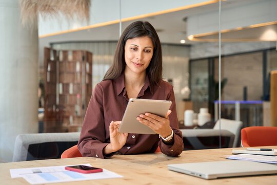 Successful smiling latin hispanic young woman using pad computer for business app. Busy executive CEO businesswoman professional holding digital tablet pc device for work in modern office workplace.