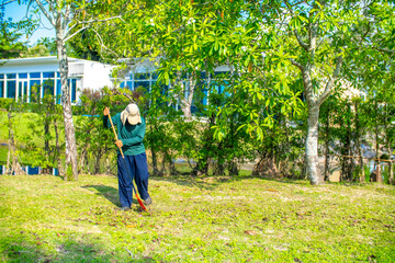 A janitor cleans the lawn area from leaves and mown grass. Hotel cleaning service.