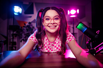 Cheerful female content creator streaming live podcast from home studio with neon lights and...