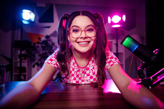 Cheerful female content creator streaming live podcast from home studio with neon lights and colorful background