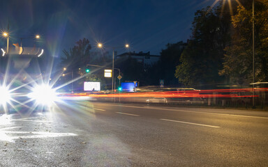 Vivid long exposure night photo of city street with bright car headlights, light trails of moving traffic, street lamps, and dark foliage