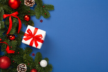 Festive Christmas tree branches with gift box on color background, top view