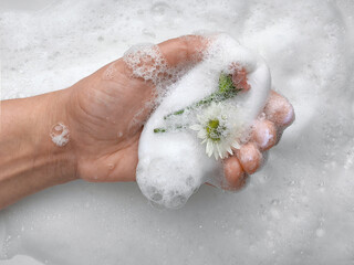 Hand holding floral soap with foam bubbles in bathroom setting