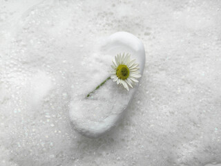 Delicate chamomile on soap among soft bubbles for spa and body care