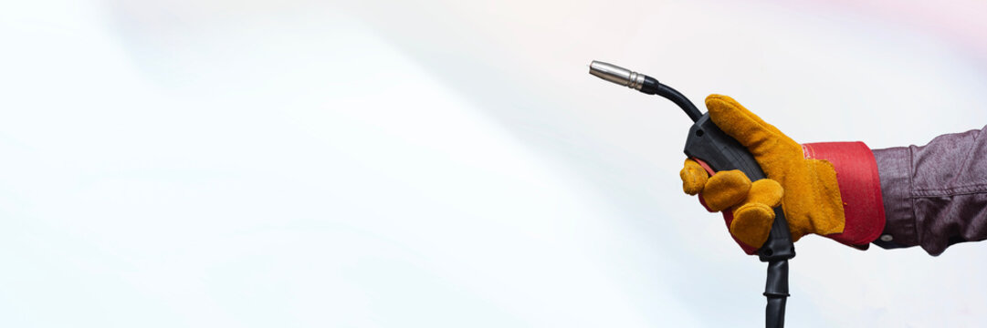 Close-up of a worker hand wearing protective gloves and holding a MIG welding torch against a clean light background. Concept of welding, industrial work and safety equipment. - Powered by Adobe