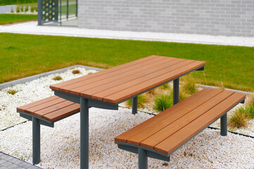 outdoor wooden picnic table in modern urban park setting, surrounded by white gravel and green grass. perfect environment for relaxation, community gatherings, or outdoor dining.