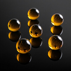 Luminous amber glass spheres or gel capsules on a black reflective surface. A modern, abstract macro concept for science, luxury cosmetics, or vitamin supplements, with dramatic lighting