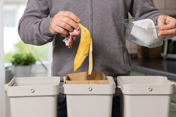 Man discarding banana peel and plastic waste into separate recycling bins, promoting sustainable waste management practices at home