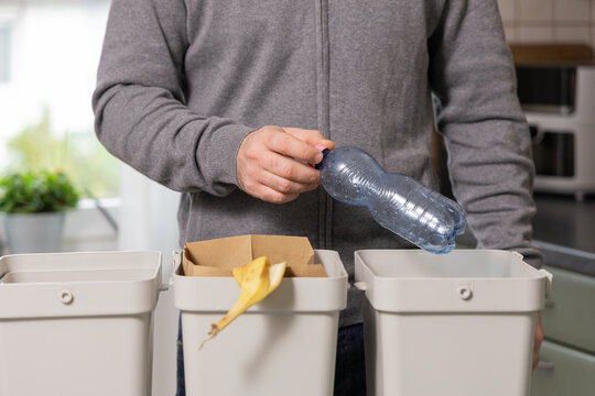 Individual sorting recyclable materials into bins at home, demonstrating commitment to recycling and sustainability practices in a modern kitchen environment - Powered by Adobe