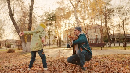 father and little child in an autumn park throw dry leaves up, happy family, live fun with dad, cheerful kid plays with foliage and parent hands throwing leaf fall, parental care of girl, nature walk