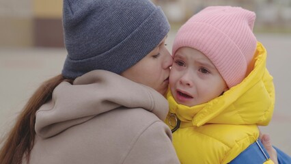 mother soothes a crying little child, mom wipes tears running down her face and hugs a kid with a backpack, educational school program, worry about lessons and grades, baby in the arms of a parent.