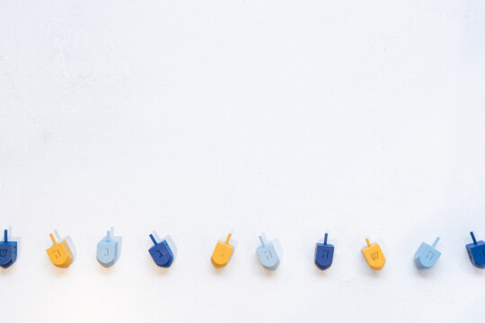 textured border background with blue and yellow wooden dreidels, which are spinning tops played in a game during the Jewish holiday of Hanukkah.