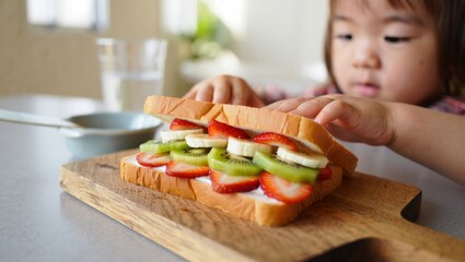 Little child preparing a healthy fruit sandwich on a wooden board, featuring fresh strawberries, kiwi, and banana slices, promoting nutritious and balanced eating for kids