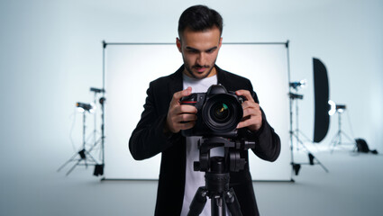 Male photographer setting up professional camera on tripod in a white cyclorama studio with lighting equipment, preparing for a commercial shoot