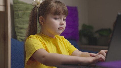 a child girl does her homework on a laptop, online distance learning on computer, schoolgirl does her homework, little kid wants to get a school education, play game on Internet, chat with classmates.