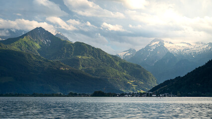 Schüttdorf lakefront panorama glows across Lake Zell, Imbachhorn to Kitzsteinhorn snowcaps under soft cloud and warm light; calm alpine mood, ideal for travel ads.