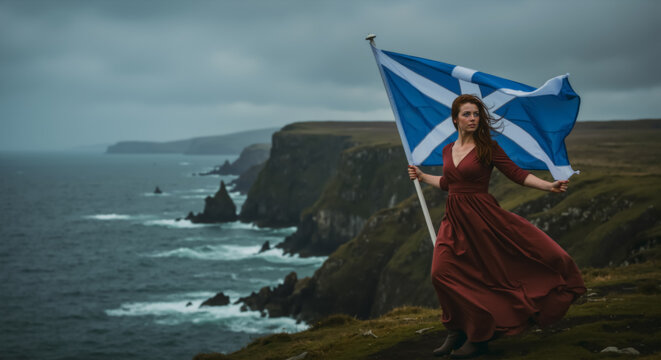 Patriotic woman with red hair holding the flag of Scotland on a windy cliff overlooking the sea. Scottish pride and heritage concept with copy space