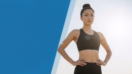 Confident athletic Asian woman in sportswear. Strong female model posing with hands on hips. Fitness and wellness concept with blue copy space
