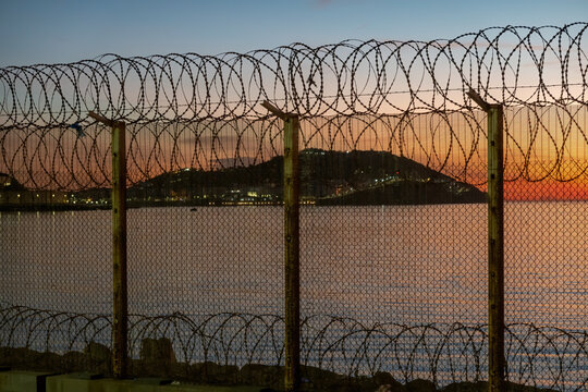 Ceuta, Spanish city in North Africa, seen from Morocco behind a thorn wire fence located on the Moroccan border against a stunning sunset over the sea. Concertina wire. Security, barrier, border