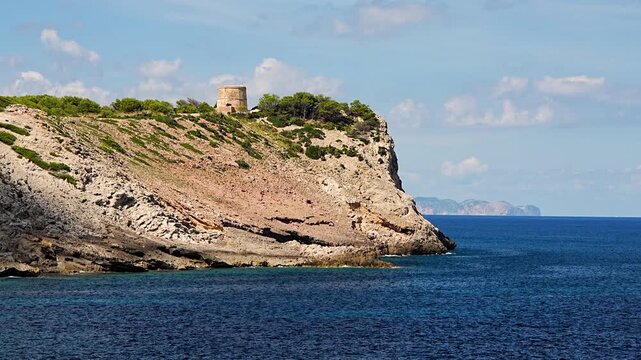 Historic stone tower Torre d Albarca on the cliffs of Mallorca, Spain. Blue sea waves and scenic Mediterranean coast in warm sunlight