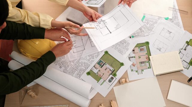 Architect and safety engineer discussion about building construction use blueprint on table with architectural document, measurement tool and wooden block scatter around at modern office. Delineation.