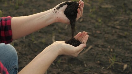 A woman farmer pours plowed land from one hand to another, preparing the fields for planting vegetables and fruit trees.