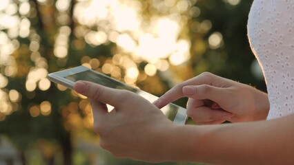 A young girl holds in her hand a modern tablet in the glare of the sunset, go online to the Internet, the rays of the sun shine on the touch screen of the tablet, the concept of modern technologies.