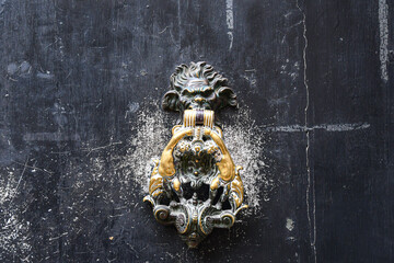 Close-up of the bronze knob of an old door, depicting the head of a man-lion creature holding in its jaws a pair of putti, Venice, Veneto, Italy