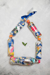Five pet plastic bottles filled with compressed plastic waste arranged in the shape of a house with green leaves inside