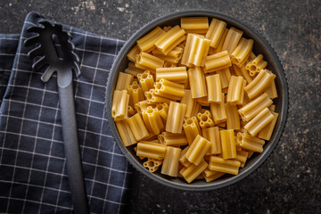 Cinque buchi. Uncooked italian pasta in bowl on black table. Top view.