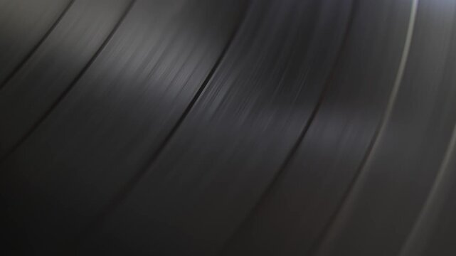 Close-up view of a black vinyl record spinning on a turntable. The grooves reflect light, creating a hypnotic and classic visual