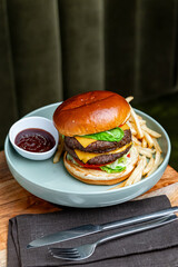 Burger with fries and ketchup on gray plate top view. Top view of cheeseburger with fries and ketchup on gray plate served over wooden table.