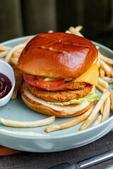 Close up of chicken burger with fries and tomato slices. Macro shot of chicken burger with lettuce, tomato, cheese and fries served with ketchup on gray plate.