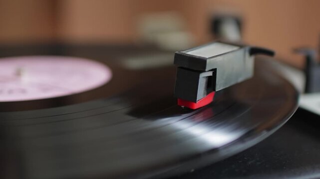 Extreme close-up of a phonograph needle dropping and riding in the grooves of a black vinyl lp spinning on a vintage record player