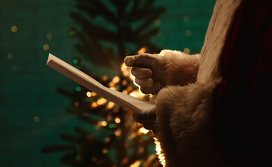 Santa Claus reads a wish list in front of a beautifully lit Christmas tree, capturing festive holiday spirit.