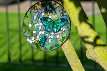 Round stained glass with colourful butterfly, sun catcher hanging on tree.
