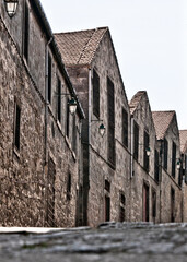 A row of old stone buildings with tiled roofs and street lamps.